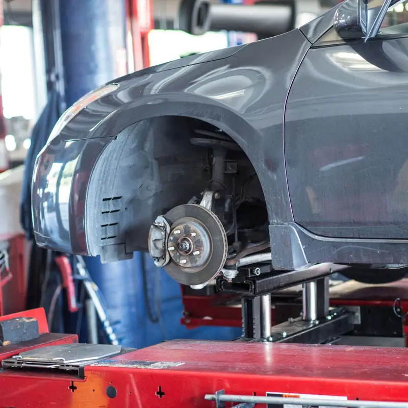 Grey car on a red lift with the wheel off and the brake rotor exposed