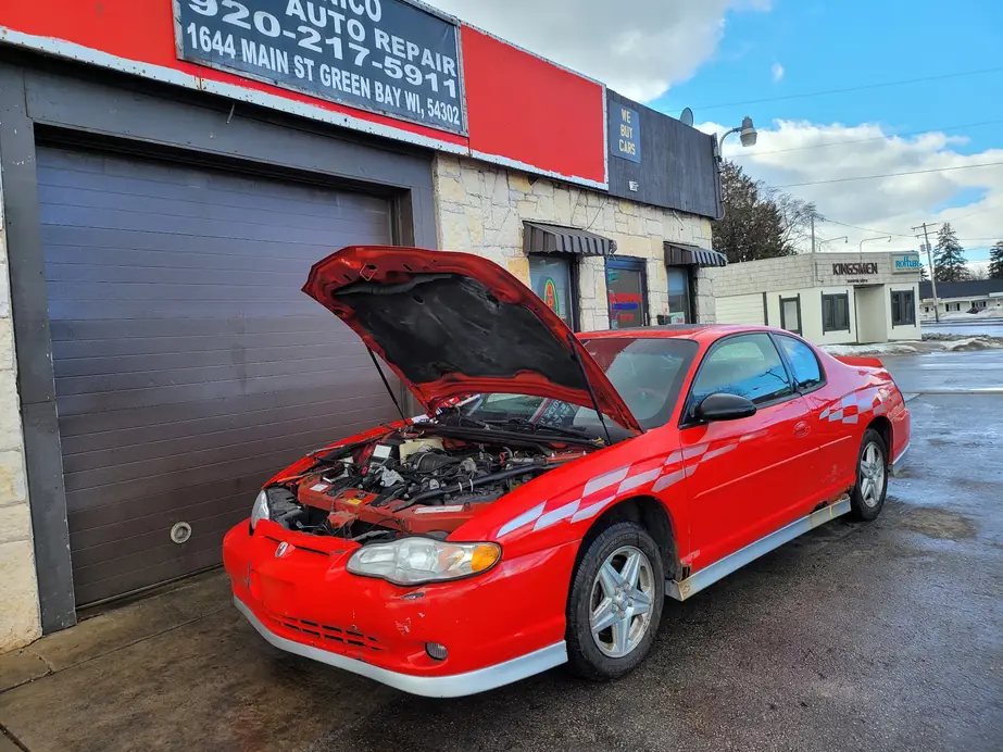 A red Monte Carlo with its hood up in front of the bay door at El Mecanico Auto Repair