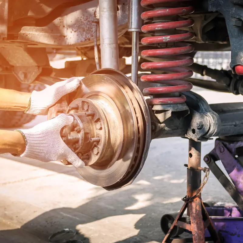 Gloved hands on a brake drum beside a red coil spring